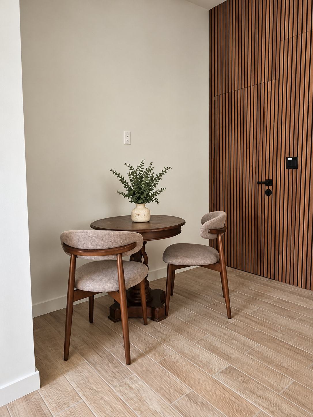 Round dining table with two chairs by the wood-slat wall
