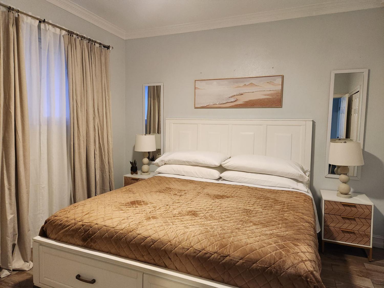 King bedroom with white panel headboard and beach artwork